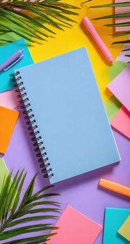 Notebook, pencils, and colored pens on colorful background with palm leaves photo