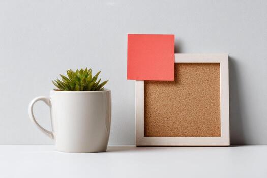 A corkboard with a red post-it note and a white mug on a white table photo