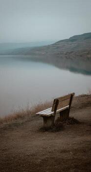 un banco sentado en un colina con vista a un lago foto