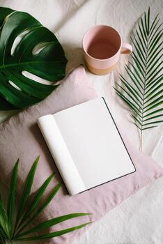 Blank notebook and coffee cup on a pink pillow with palm leaves photo