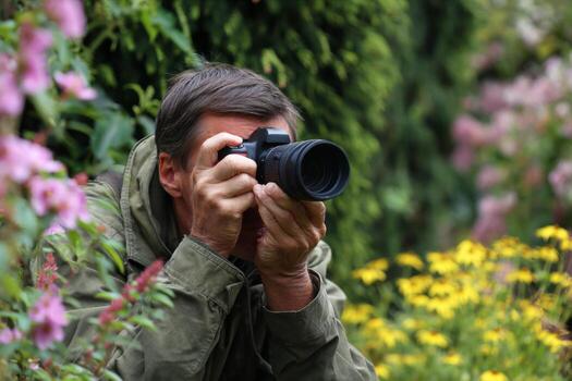A man with a camera focuses intently on capturing images of wildlife among blooming flowers in a lush garden on a warm summer afternoon. Nature surrounds him photo