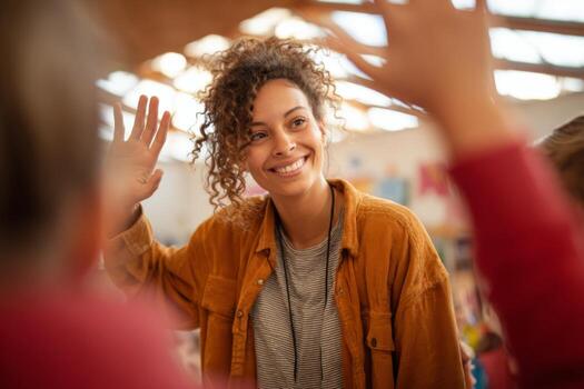 A teacher with curly hair smiles as she interacts with students in a vibrant classroom filled with colorful learning materials. The atmosphere is lively and encouraging photo