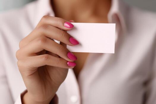 A woman is showcasing a blank card in her hand, displaying neatly manicured pink nails. The background suggests a professional office atmosphere with soft lighting photo