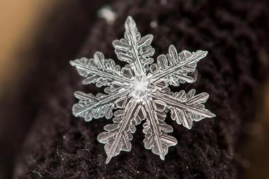 A stunning snowflake lands softly on a dark woolen glove, displaying its complex and unique crystalline structure in vibrant detail, showcasing the beauty of winters intricacies photo