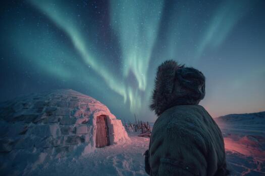 A person observes the vibrant northern lights illuminating the sky above an igloo in a snowy setting during dusk. The colors create a magical atmosphere in the wilderness photo