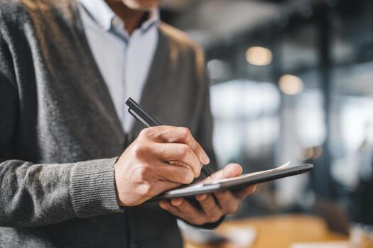 An office worker actively takes notes during a meeting, utilizing a smart pen on a tablet to digitize handwritten content in a contemporary office setting photo
