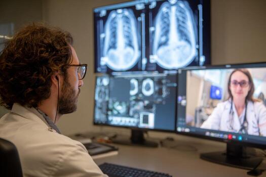 Radiologist engages in a virtual consultation with a patient, analyzing CT images displayed on dual screens in a contemporary medical setting. High definition resolution captures the details clearly photo