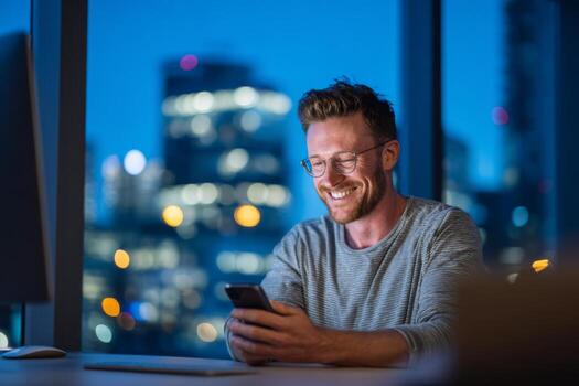 en un moderno oficina, un hombre se sienta a un escritorio sonriente mientras mirando a su teléfono inteligente el ciudad horizonte brilla en el antecedentes como noche conjuntos en, creando un calentar atmósfera foto