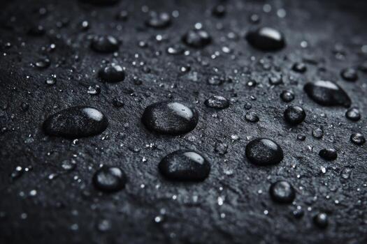 Water droplets rest on a smooth dark stone surface, reflecting light as they gather in clusters. The scene captures the essence of a rainy evening, emphasizing the beauty of nature photo