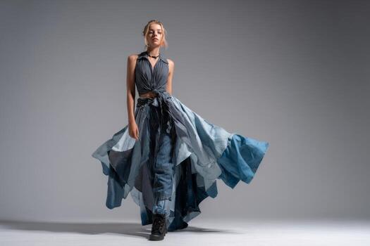 A model showcases a striking outfit made of flowing blue fabrics in a studio setting. The design blends various patterns, enhancing the dramatic effect as she walks photo