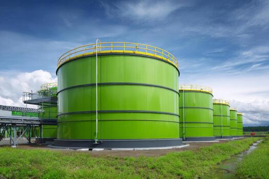 Bright green storage tanks are arranged in a row at an industrial site. The sky is partly cloudy, creating a striking backdrop for the large structures photo