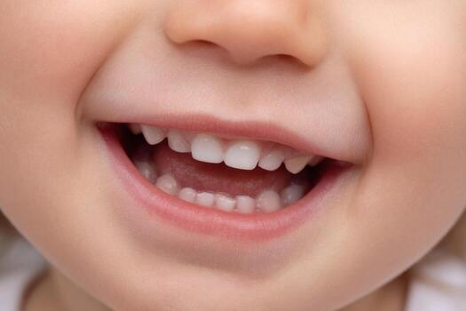 A joyful child beams with a wide smile, displaying a set of baby teeth during a playful moment indoors in warm lighting. The expression radiates happiness and innocence photo