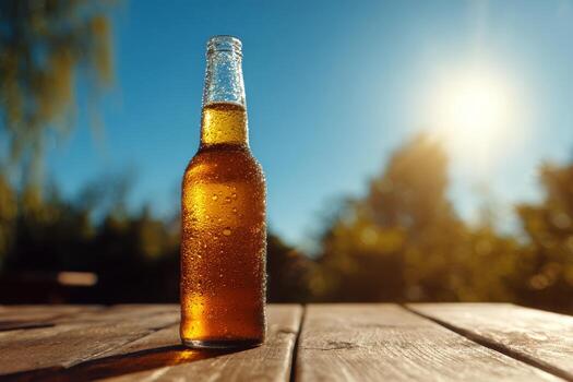 A glass bottle filled with a golden beverage stands on a rustic wooden table, glistening with condensation. Sunlight shines brightly, creating a warm and inviting atmosphere in the garden photo