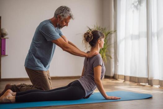An instructor guides a student through a yoga pose in a well-lit studio. Natural light streams in, creating a calm atmosphere perfect for practice. Both focus on alignment and breath photo