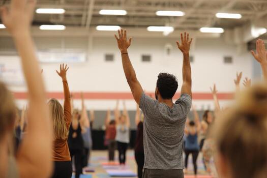 Participants are engaged in a yoga class in a large gym. A diverse group practices together, focusing on mindfulness and stretching under overhead lights photo