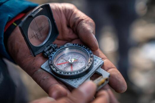 A person holds a compass in their hand, carefully checking their direction while exploring a mountain trail. The early morning sun casts soft shadows, enhancing the landscape photo