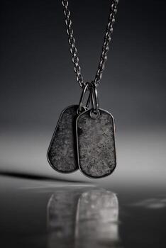 Two grey, worn metal tags hang from a chain against a dark, reflective background photo