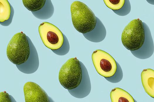 Overhead shot of numerous avocados, whole and halved, on a light blue background photo