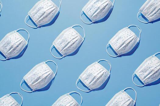 Patterned composition of disposable face coverings on a light blue background photo