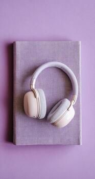 Pastel-colored headphones rest atop a textured purple notebook, set against a solid purple background photo