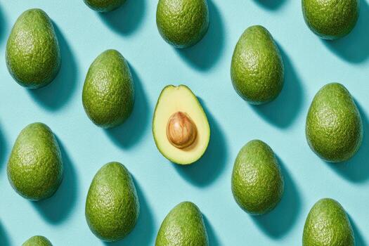 Overhead shot of whole avocados arranged with one halved on a vibrant blue surface photo