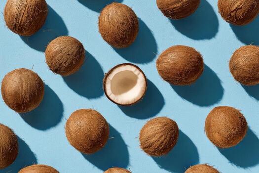 A grid of coconuts, one cut open, cast long shadows on a light blue surface photo