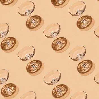 Diagonal repeating pattern of empty stemmed glasses casting distinct shadows on a beige surface photo