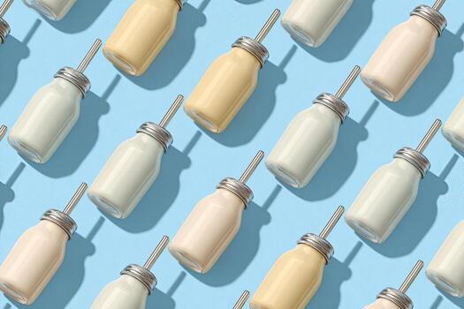 Angled pattern of beverage bottles on a pastel blue surface, with straws photo