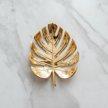 Gleaming gold leaf-shaped dish with intricate details resting on a pristine marble surface photo