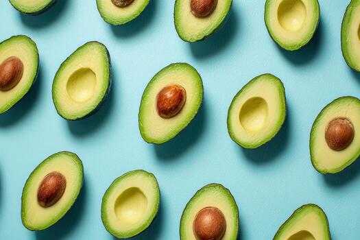 Overhead shot of numerous avocado halves, arranged in a repetitive, diagonal pattern on a blue background photo