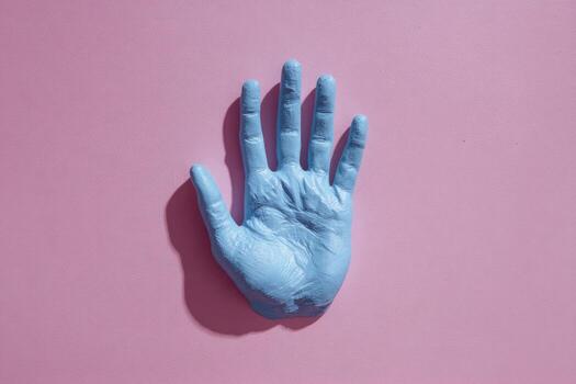 Blue painted hand pressed flat on a pink surface casting a shadow photo
