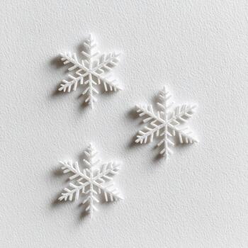 Three white decorative snowflakes on a textured, light-toned surface, top-down view photo
