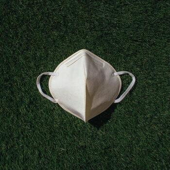 A white face mask with ear loops rests atop vibrant green grass, centered photo