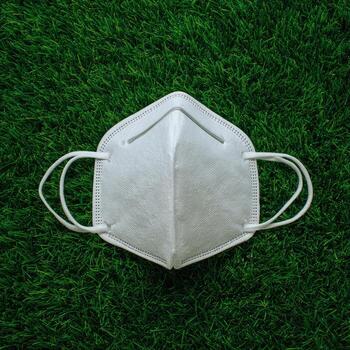 White respiratory mask on green grass, top-down view, focused photo
