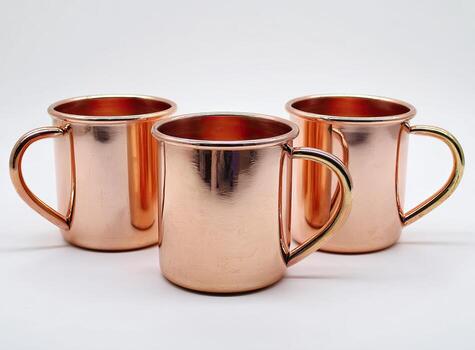Three shiny, copper-colored mugs with curved handles arranged on a plain white surface photo