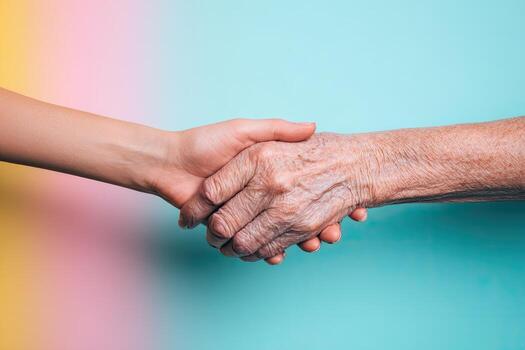 Close-up shot of two hands shaking, one youthful, the other aged. Colorful background photo