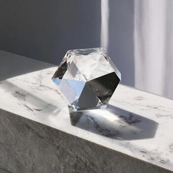 A faceted, clear geometric object sits on a marble surface, lit by sunlight. Shadows play photo