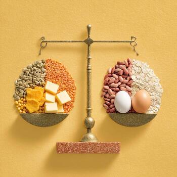 A golden scale balanced atop a mustard-yellow surface. Various food items are arranged on either side of the scale, representing a nutritional comparison photo