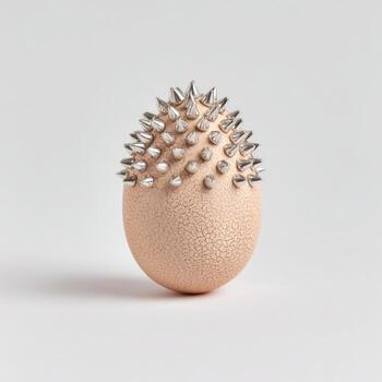 An egg-shaped object, skin-toned, with metallic spikes covering the top, set on a white background photo