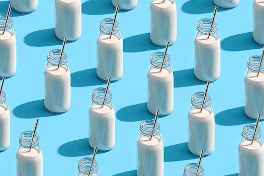 Patterned bottles of white liquid with straws against a blue background, casting crisp shadows photo
