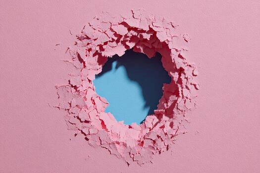 A hole ripped in pink surface revealing blue background with textured, uneven edges photo