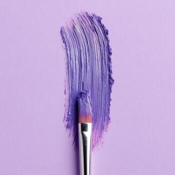 Makeup brush creating a purple swipe on a matching background, close up photo