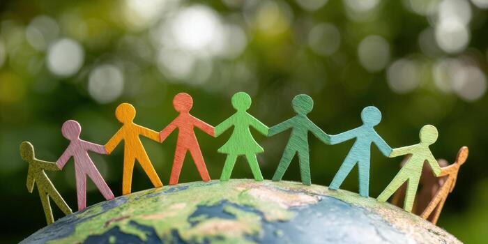 Group of diverse people holding hands, standing on top of the Earth with a green bokeh nature background. Unity and global connection for World People's Day. Paper figures representing human diversity photo