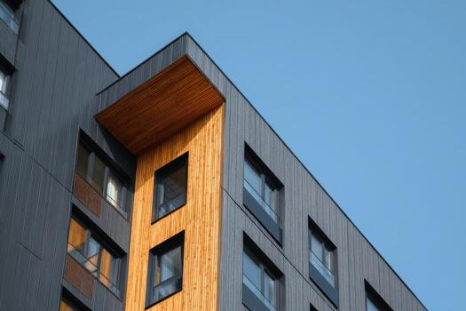 Building facade with black and brown cladding. Dark grey metal cladding with wood panels finish on apartment block. Bottom view. Blue sky. Timber paneling on modern architectural design urban setting photo
