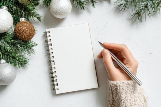 Woman's hand writing in empty notebook at the desk with Christmas decoration. Back to life, goal list. Plan, goals, checklist, idea concept. Top view, copy space. New Year. Blank White Paper Sheet. photo