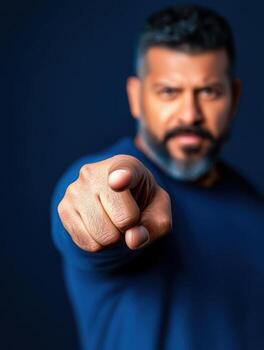 Confident man pointing at camera with blue background, strong expression and engagement photo