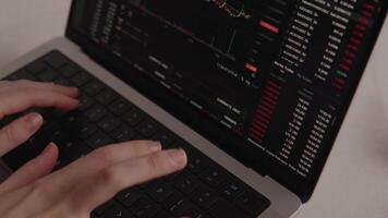 Hands typing on laptop keyboard with cryptocurrency trading platform open, showing candlestick charts, red numbers, and live market data for online investment and analysis video