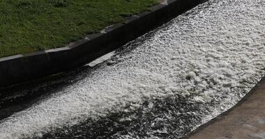 ein Überlauf auf ein Damm Erstellen ein turbulent fließen von Wasser mit Weiß Schaum im ein Beton Kanal. video