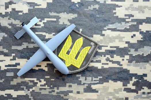 Unnamed grey toy drone model and Ukrainian Armed Force patch on camouflage fabric photo