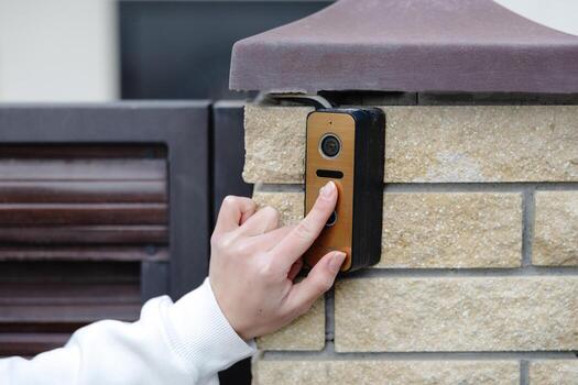 mujer prensado botón en moderno intercomunicador sistema a edificio entrada. foto